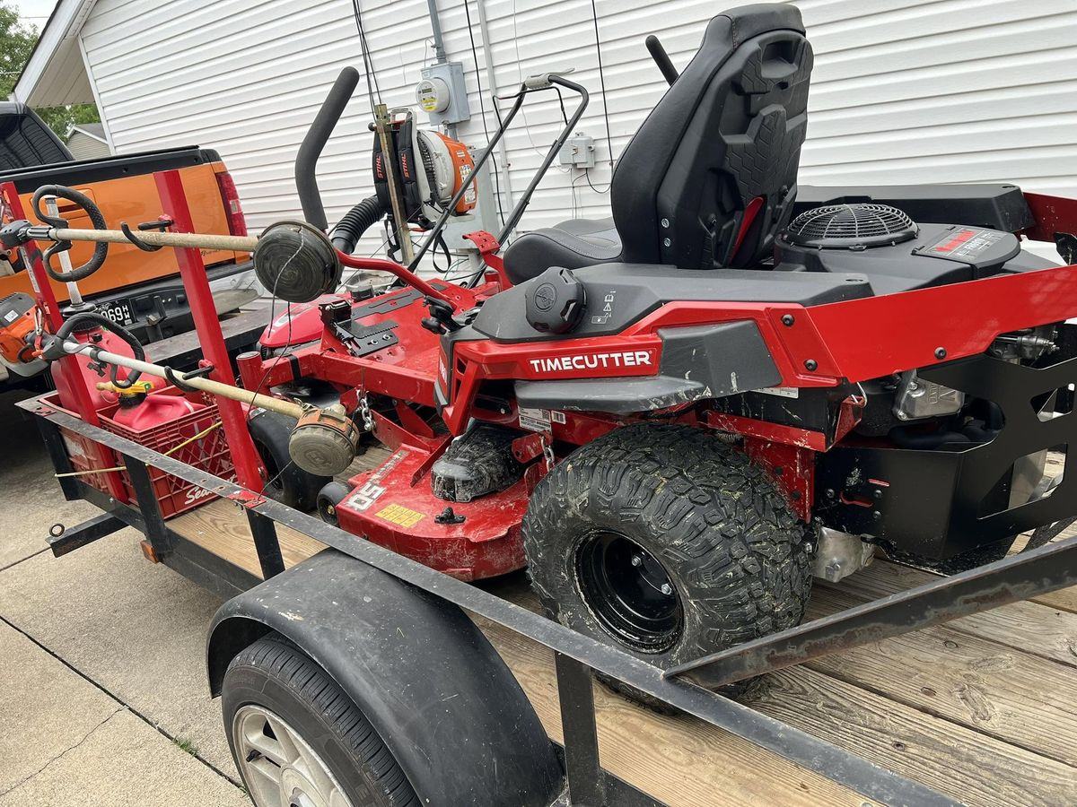 The red Toro TimeCutter strapped down on the open trailer, Stihl trimmers racked beside it